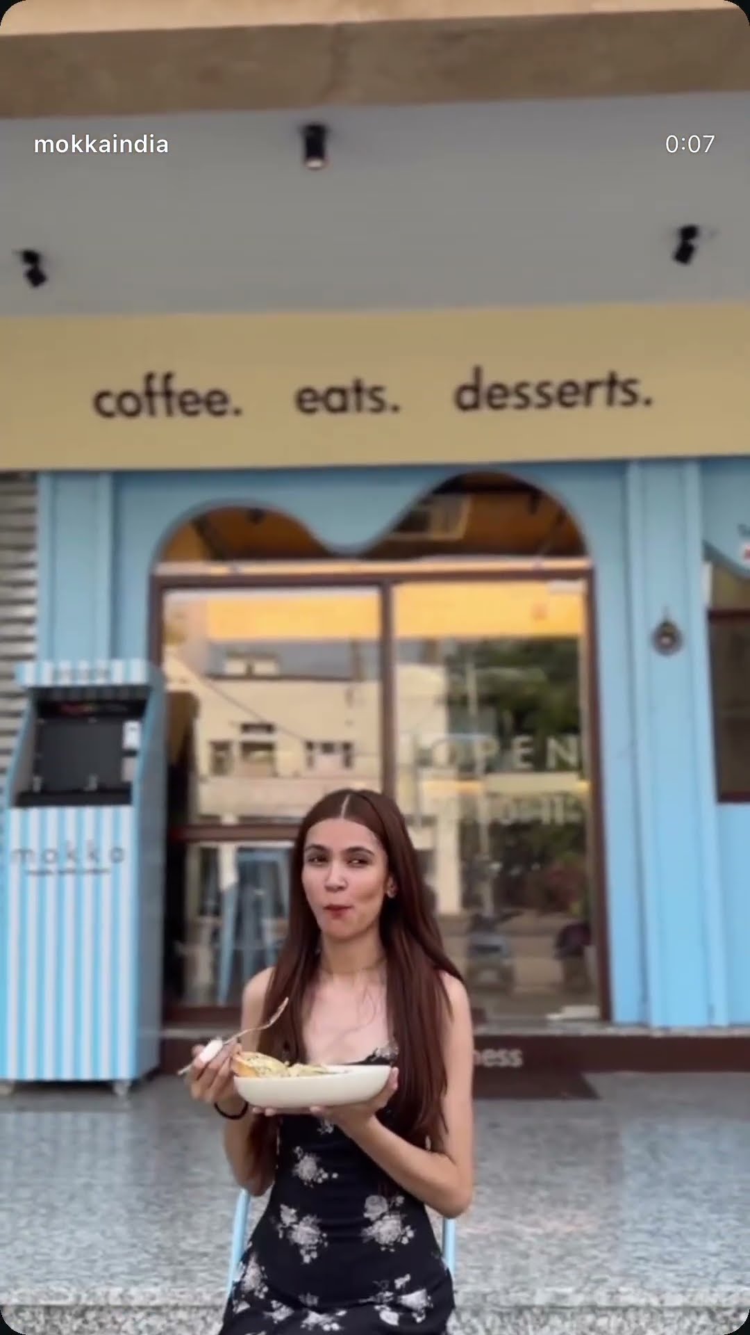 A creator outside a cafe storefront lettered coffee, eats, desserts