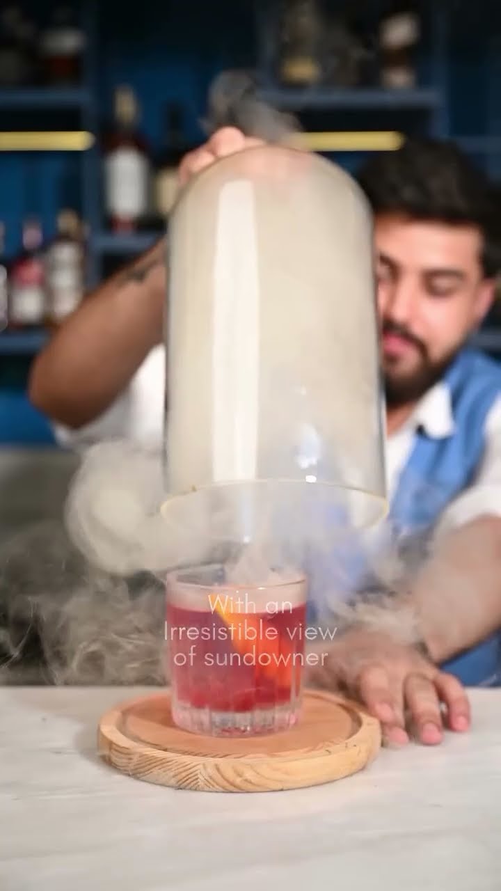 Two bartenders lifting a smoke-filled cloche from a cocktail