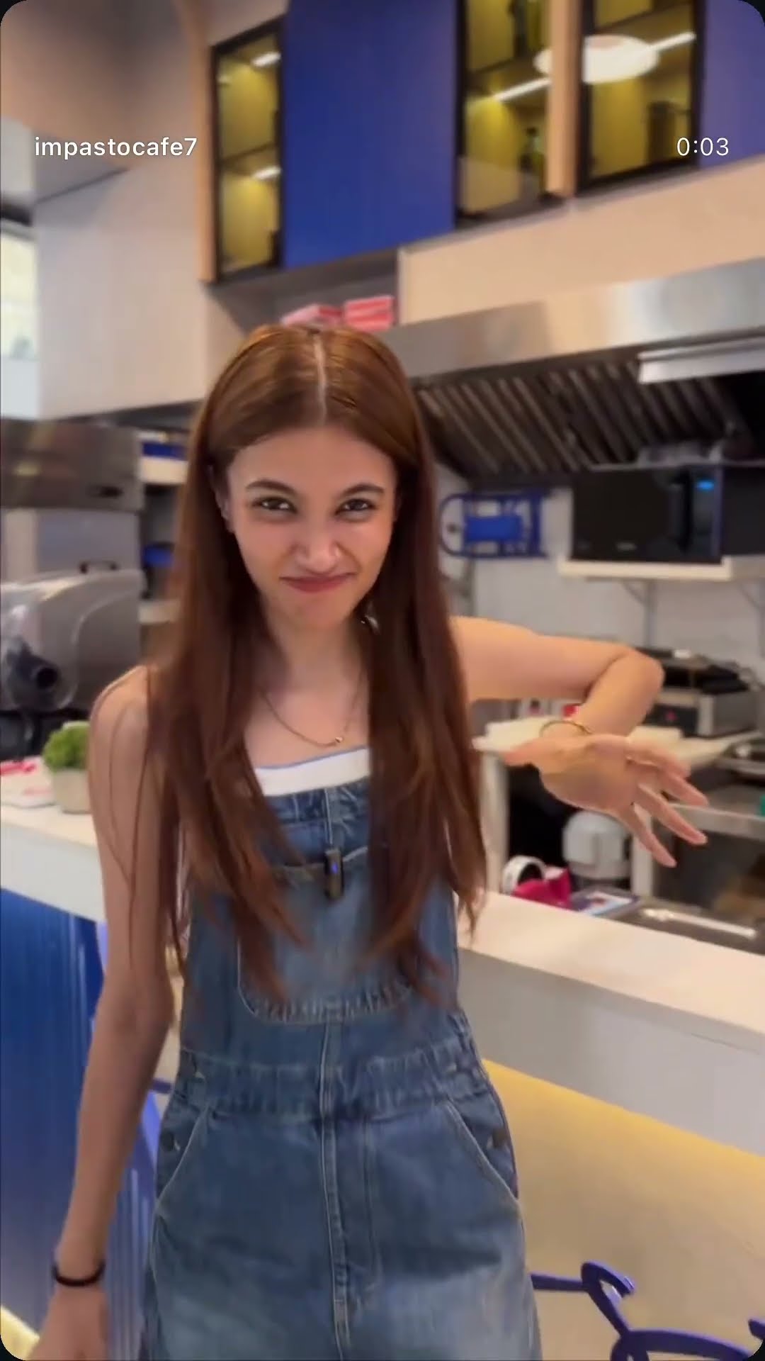 A creator in denim dungarees gesturing at a cafe counter