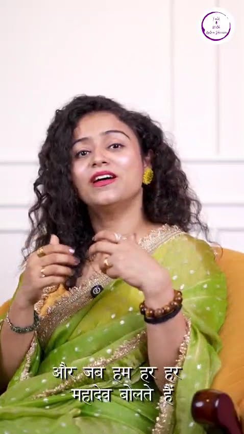 A woman in a green sari speaking to camera with Hindi subtitles across the frame