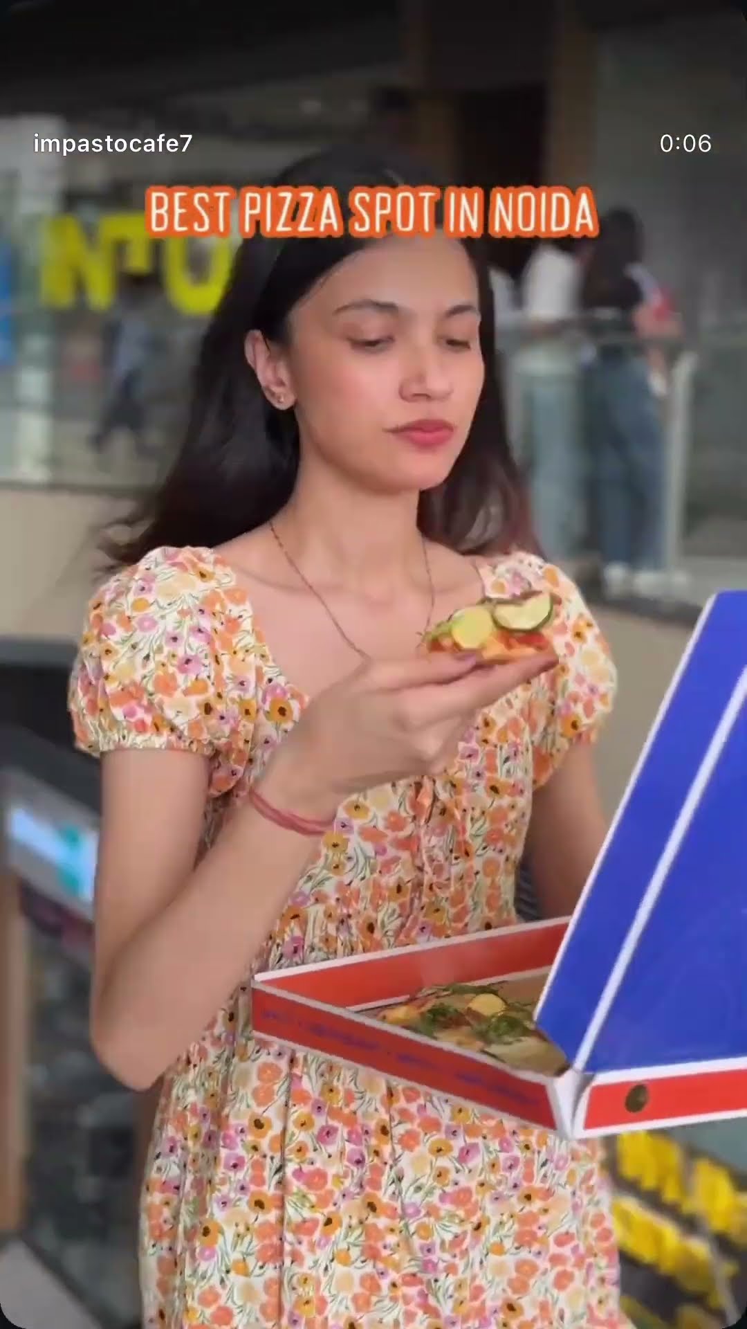 A creator in a floral dress holding an open pizza box to camera