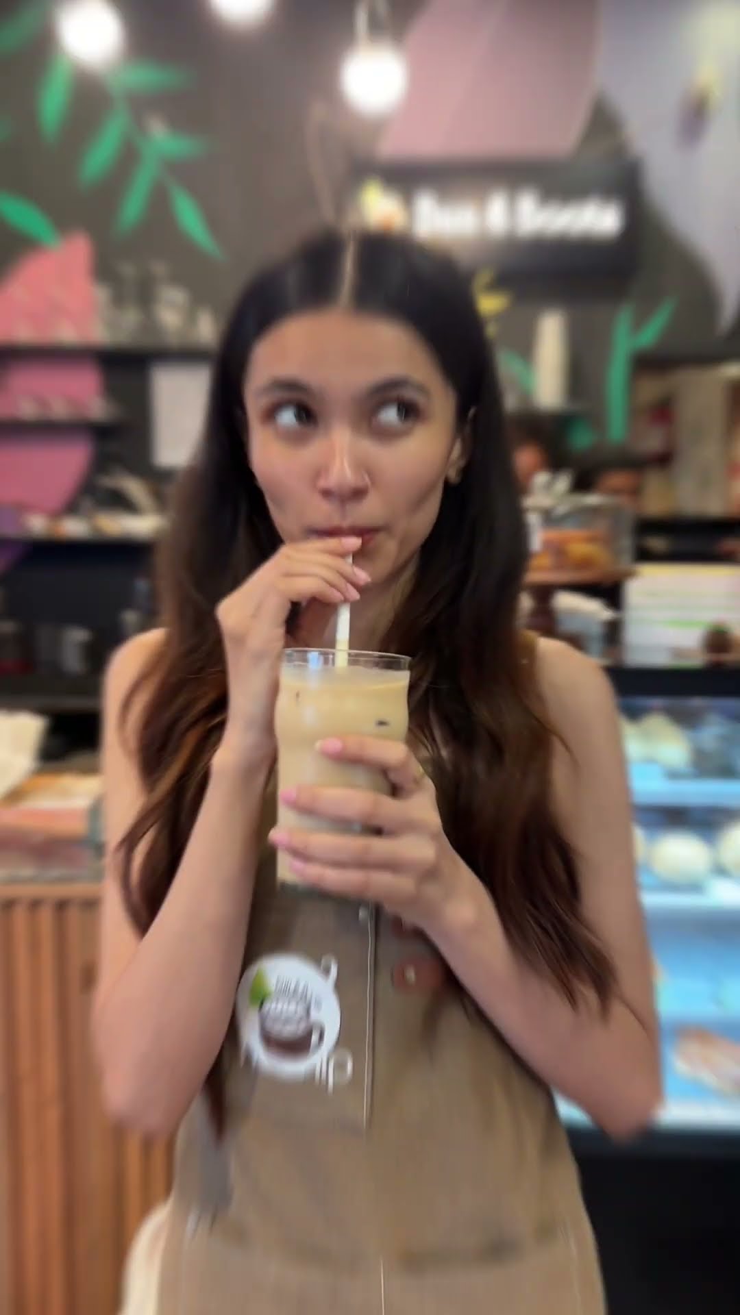 A creator drinking an iced coffee inside a plant-filled cafe